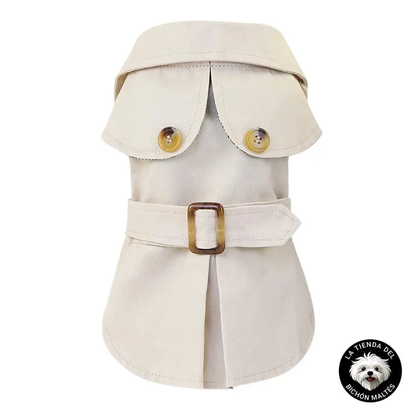 Una Gabardina para Bichón Maltés en color beige, que recuerda a una gabardina con solapas abotonadas y un cinturón con hebilla de latón en la cintura, es perfecta para tu Bichón Maltés. Presentado sobre un fondo blanco, incluye un emblema circular con un perro pequeño y el texto "LA TIENDA DEL BICHON MALTÉS" en la esquina inferior derecha.