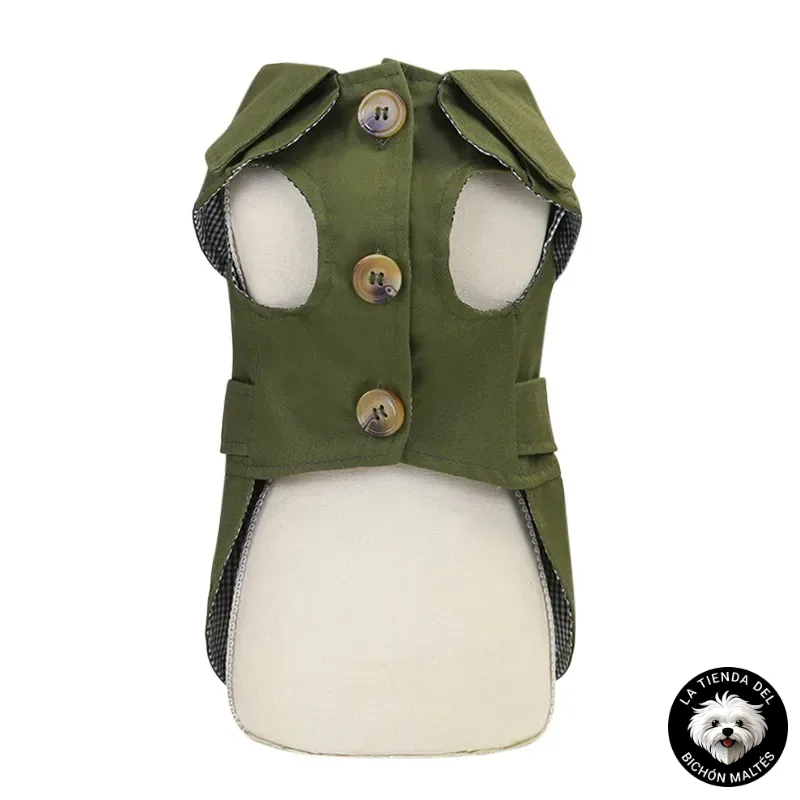 Un chaleco para perros pequeño, verde, abotonado y con tres botones grandes, diseñado como una Gabardina para Bichón Maltés - Varios Colores. El chaleco presenta un frente y laterales abiertos para facilitar el ajuste. El logo en blanco y negro de "La Tienda del Bichón Maltés" con una caricatura de Bichón Maltés está en la esquina inferior derecha.